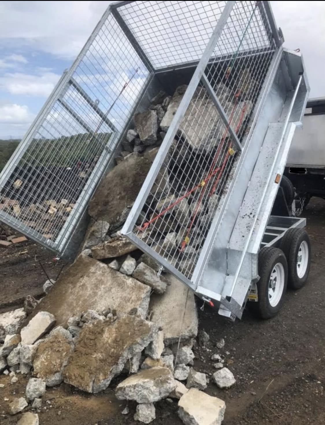 Galvanised caged tipper trailer tipping a load of broken concrete