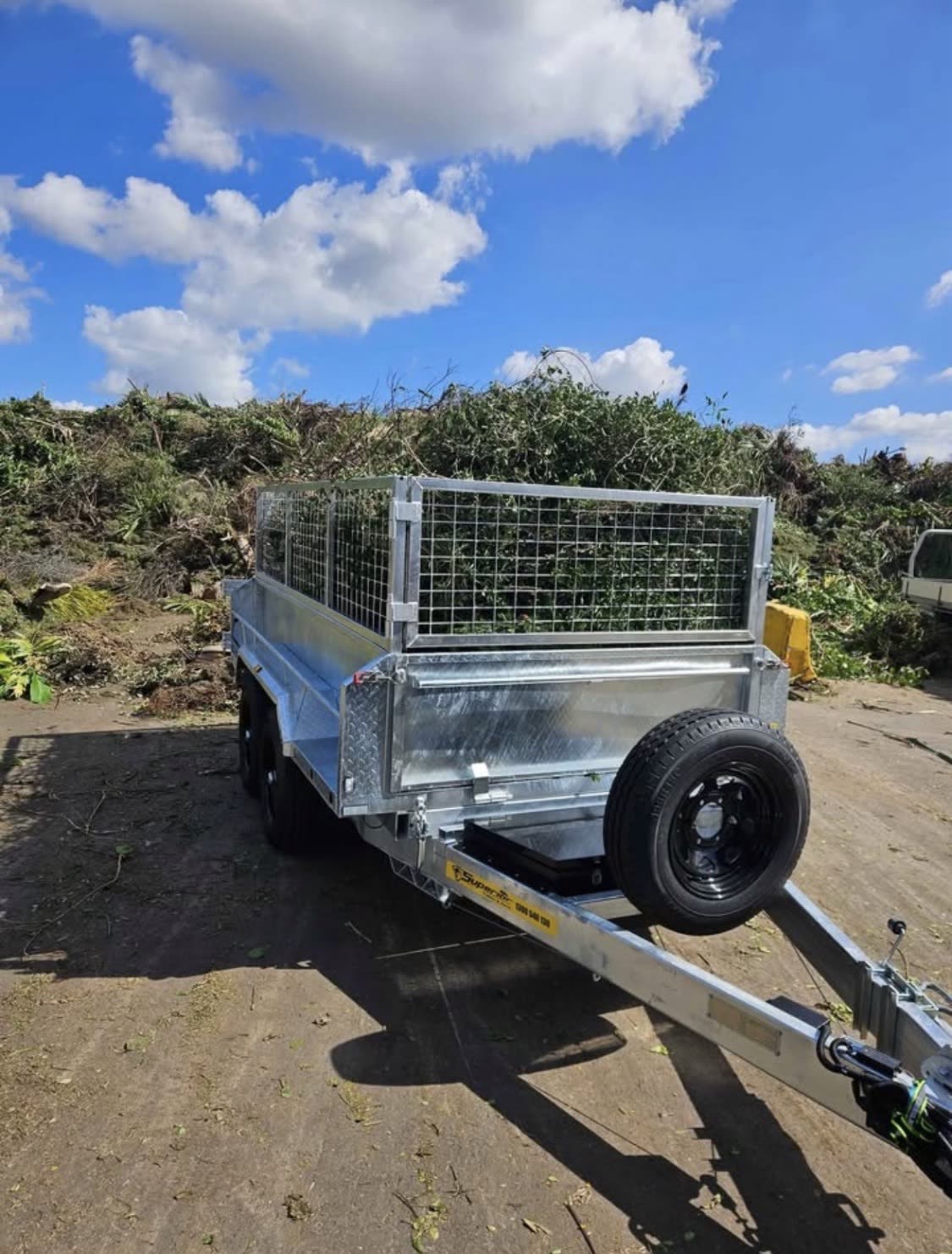 Galvanised tandem tipper trailer with mesh cage loaded with green waste